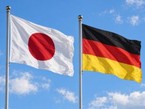 Die Flaggen Japans und Deutschlands wehen nebeneinander an zwei Fahnenmasten vor blauem Himmel
