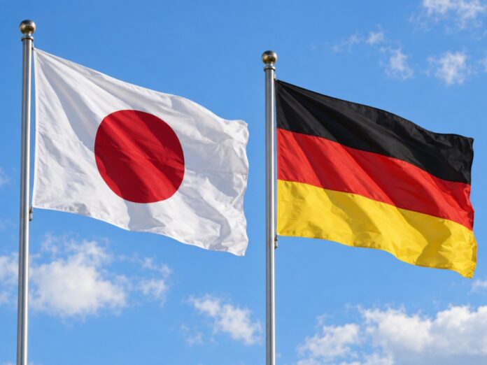 Die Flaggen Japans und Deutschlands wehen nebeneinander an zwei Fahnenmasten vor blauem Himmel