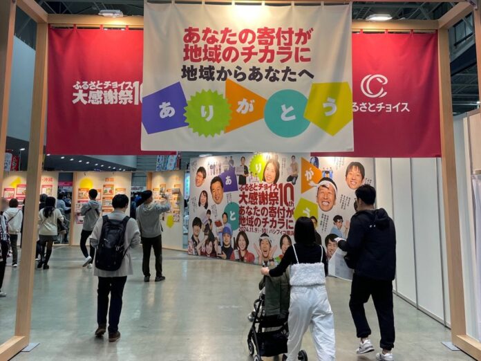 Eingang einer Messe des Portals Furusato Choice mit Bannern, Besucher gehen hinein