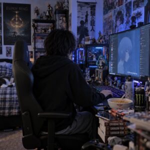 Junger Mann von hinten an seinem Computer in einem abgedunkelten Zimmer