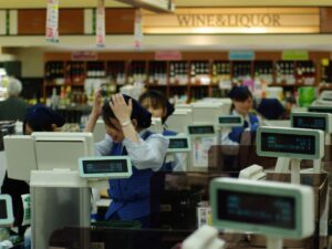 Kassiererin in einem japanischen Supermarkt fasst sich mit beiden Händen an den Kopf, daneben weitere Kassen
