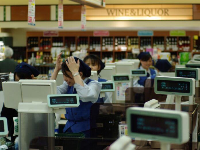 Kassiererin in einem japanischen Supermarkt fasst sich mit beiden Händen an den Kopf, daneben weitere Kassen