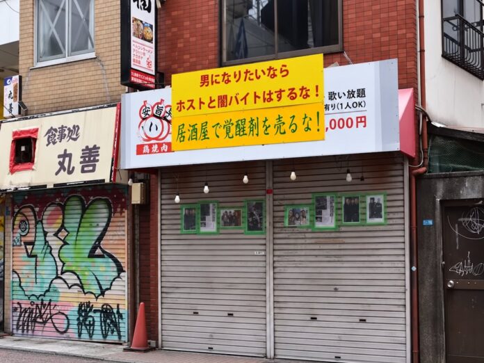 Geschlossene Ladenfront in Nishinari mit einem gelben Schild, auf dem vor Host-Jobs, Schattenjobs und Drogenhandel gewarnt wird