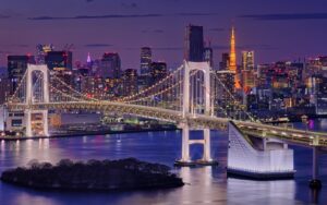 Blick vom Strand in Odaiba auf die Rainbow Bridge und die Skyline Tokios in der Abenddämmerung
