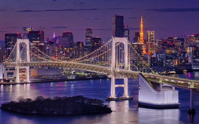 Blick vom Strand in Odaiba auf die Rainbow Bridge und die Skyline Tokios in der Abenddämmerung