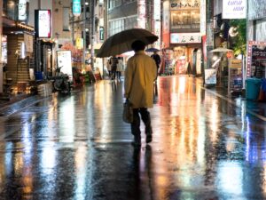 Ein Mensch mit Schirm geht nachts allein durch eine regennasse Gasse in Tokio