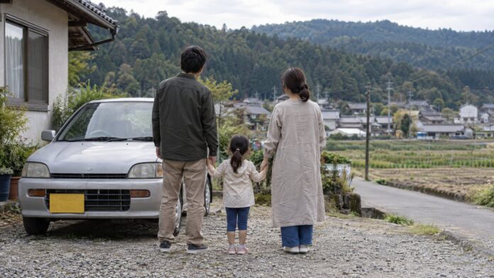 Familie mit Kind neben einem alten Kleinwagen in einem japanischen Dorf