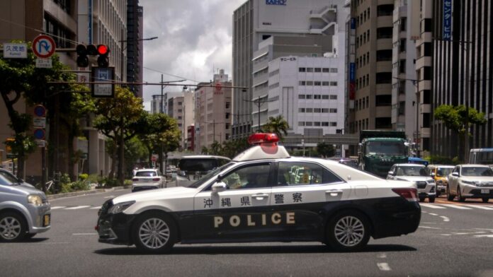 Symbolbild: Weiß-schwarzer Streifenwagen der Präfekturpolizei Okinawa mit der Aufschrift POLICE auf einer Kreuzung in Naha