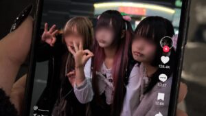 Hand hält ein Smartphone mit einem TikTok-Video: drei Jugendliche im Jirai-Stil mit unkenntlich gemachten Gesichtern posieren nachts in Kabukichō
